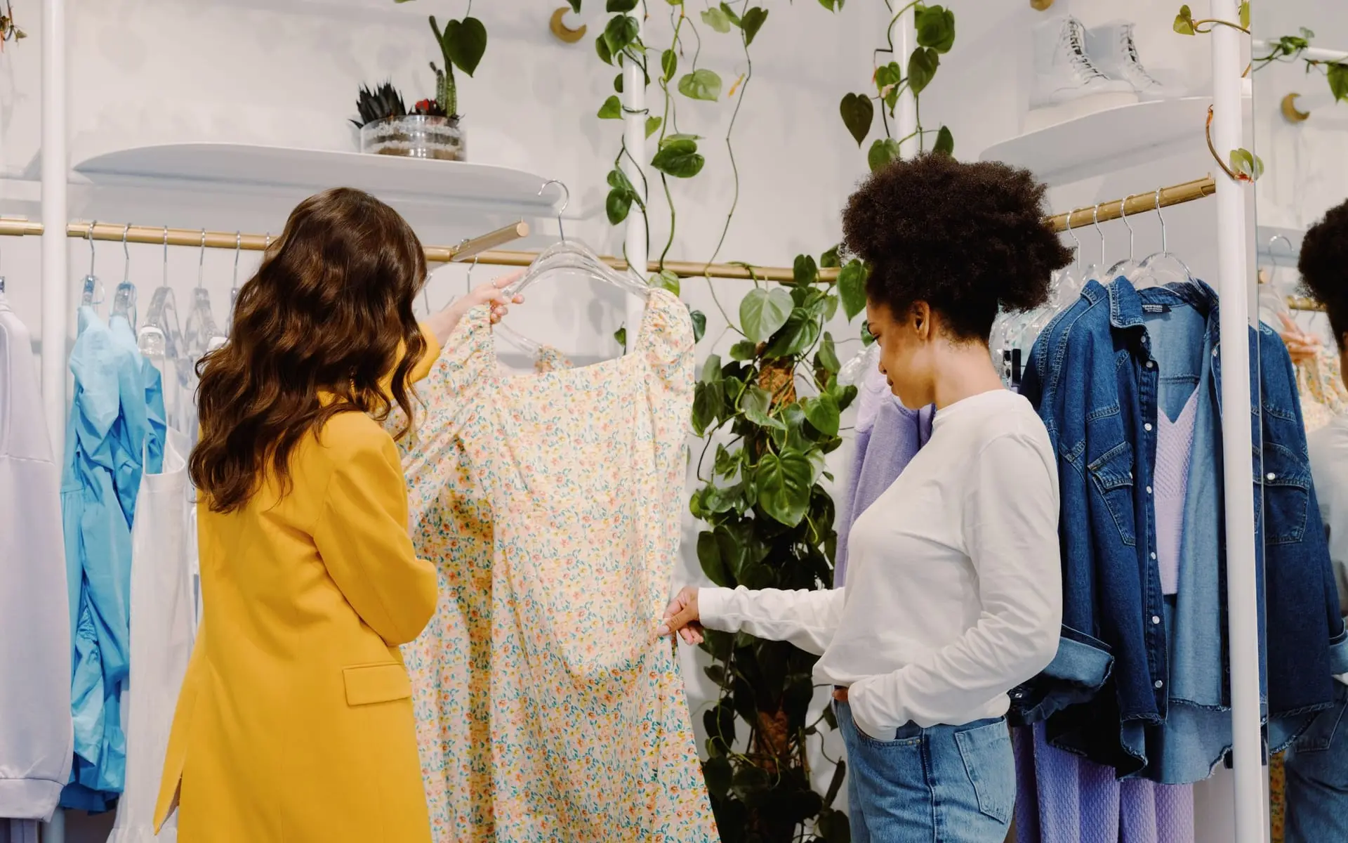 Dos mujeres revisan un vestido floral en una boutique de ropa con plantas colgantes