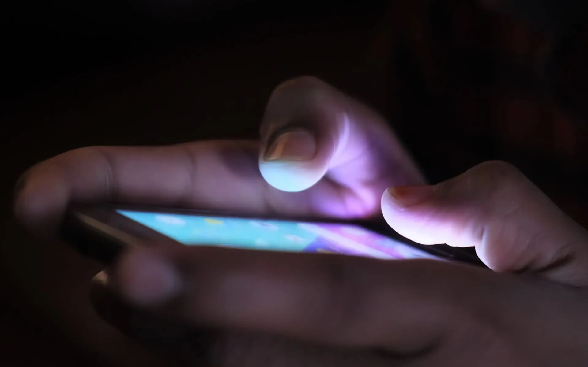 Dedos tocan la pantalla luminosa de un celular en una habitación oscura