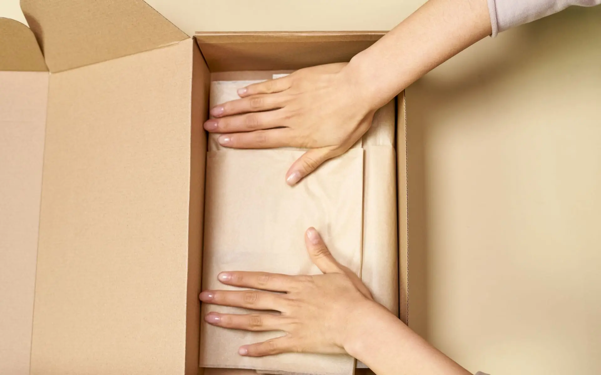 Manos acomodan papel de embalaje dentro de una caja de cartón abierta para preparar un envío