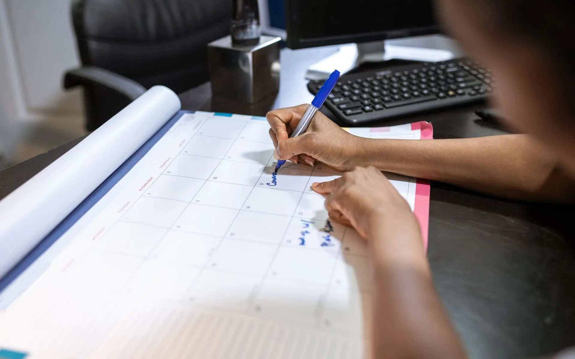 Persona escribe con marcador azul sobre un calendario mensual extendido en el escritorio