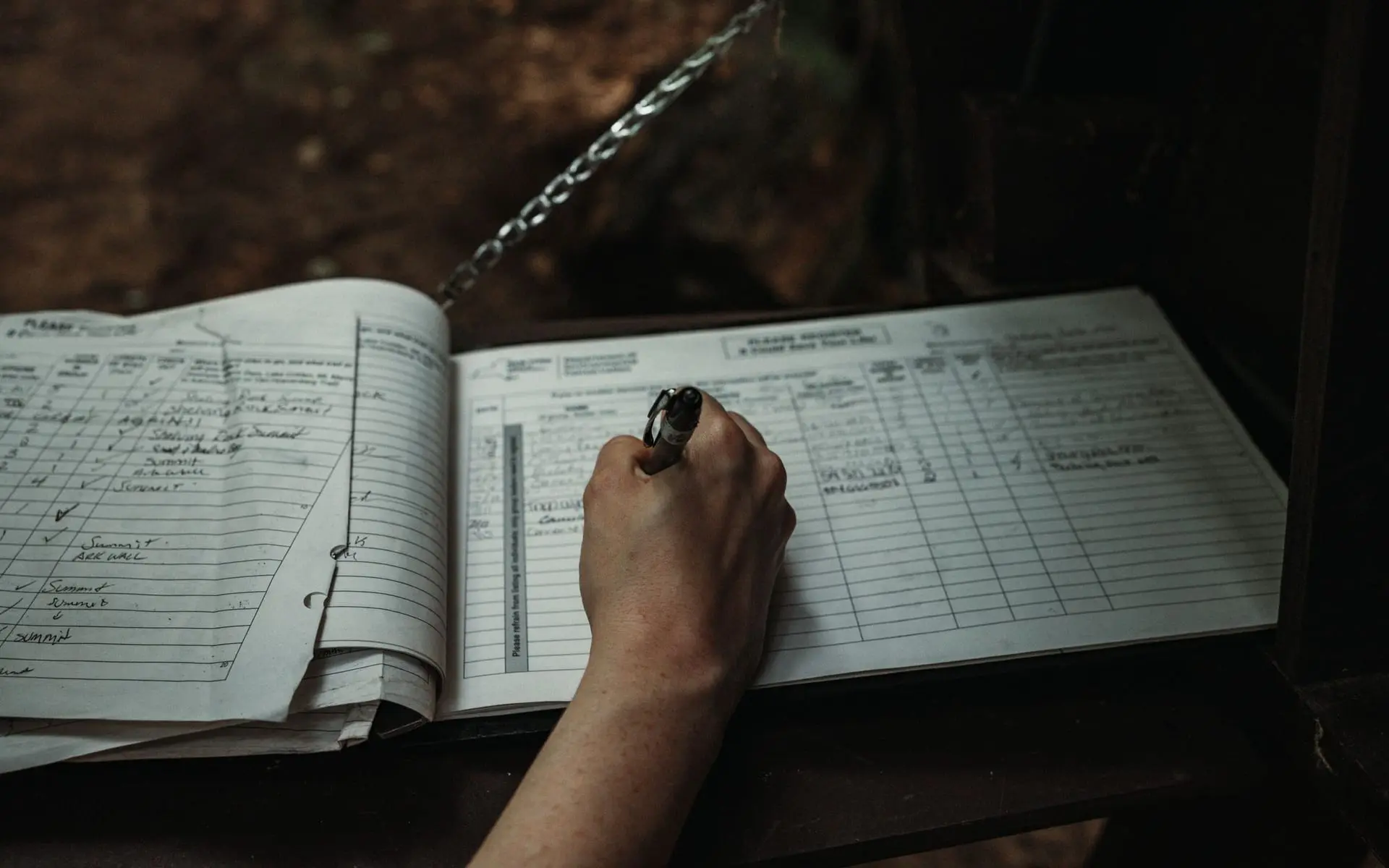 Mano con bolígrafo diligenciando un libro de registro en papel con columnas y filas