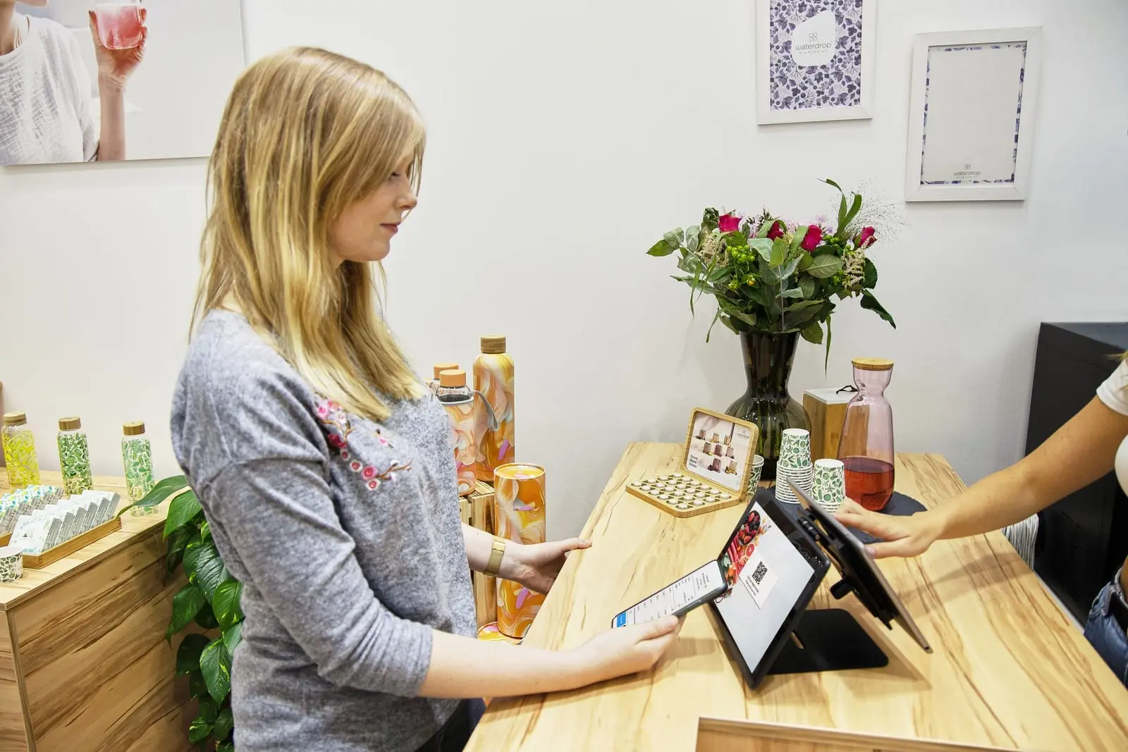 Mujer sostiene un celular junto a una tableta sobre el mostrador de madera de una tienda con flores