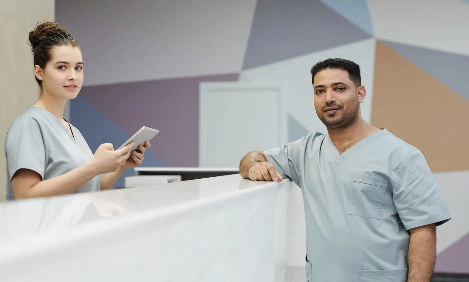 Dos funcionarios de salud con uniforme atienden en una recepción con una tableta