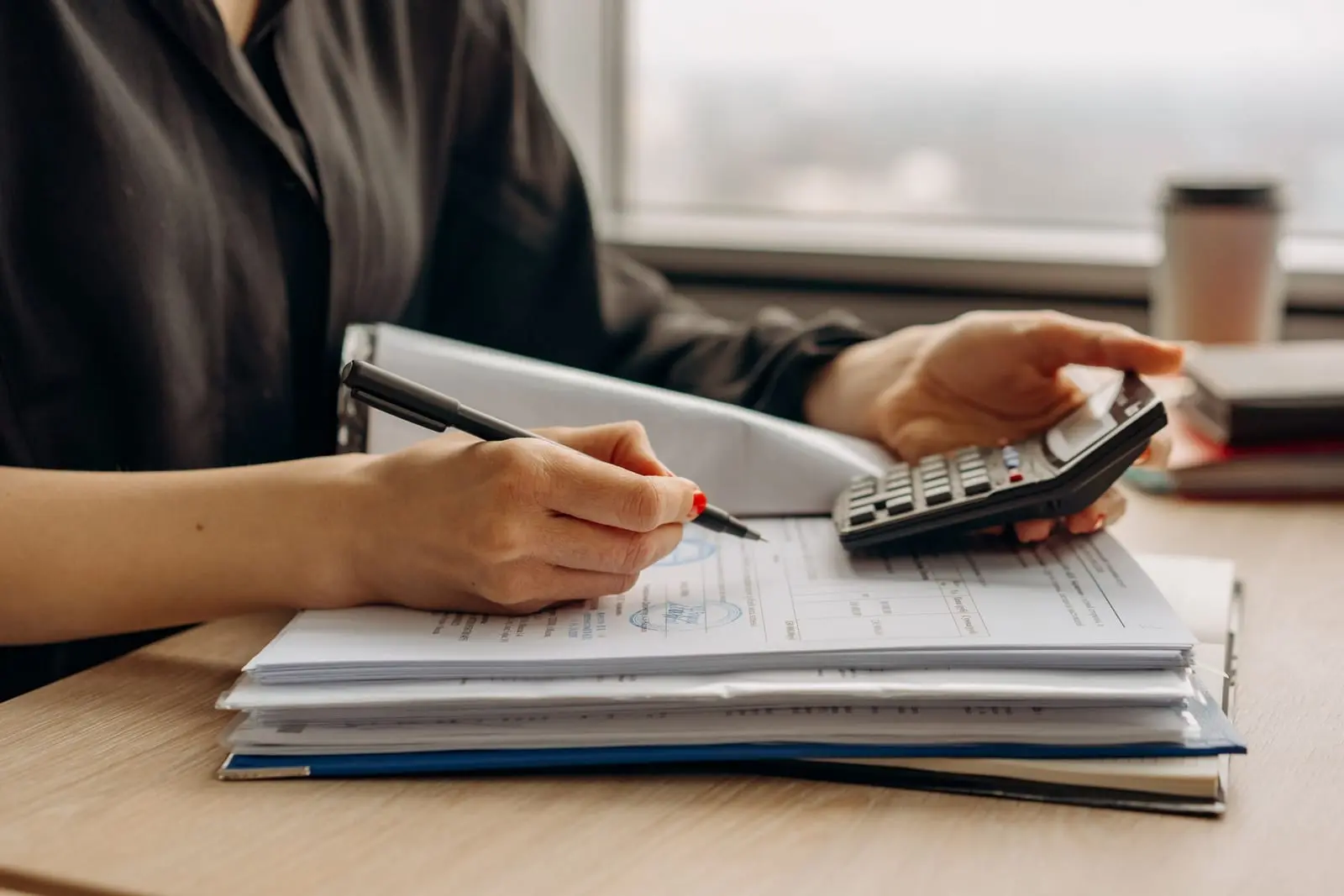Manos con calculadora y bolígrafo revisan documentos sobre un escritorio para preparar una cotización