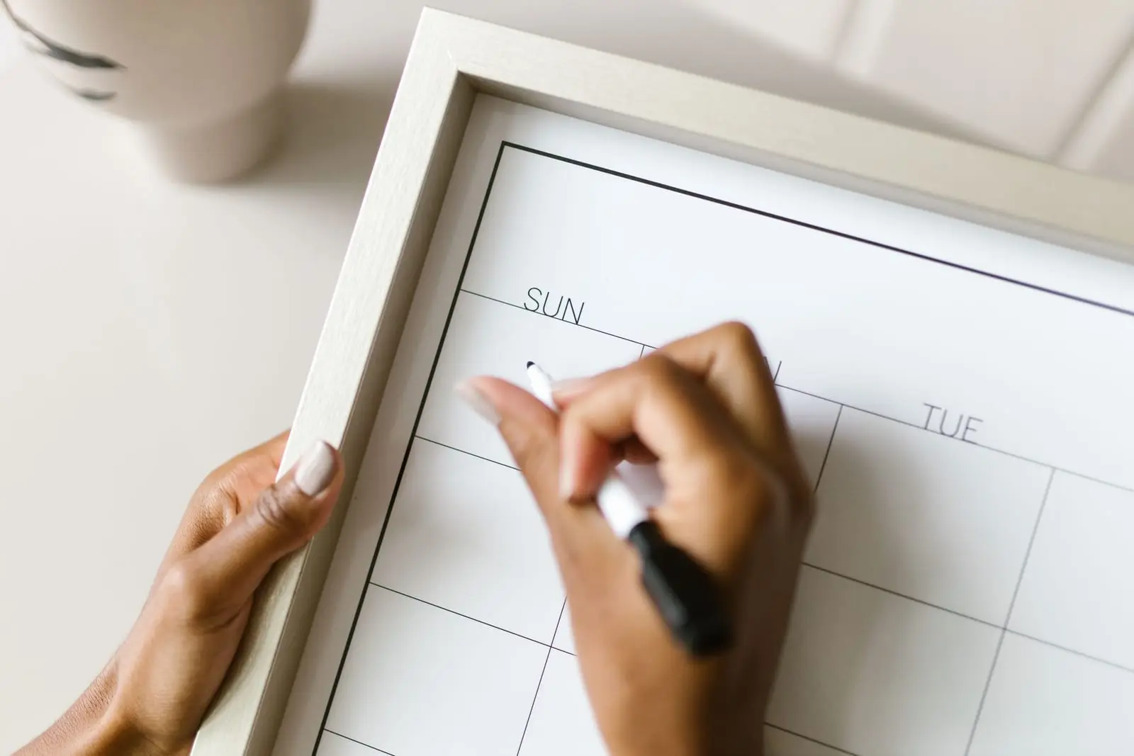 Manos escribiendo en un calendario semanal enmarcado de pizarra blanca
