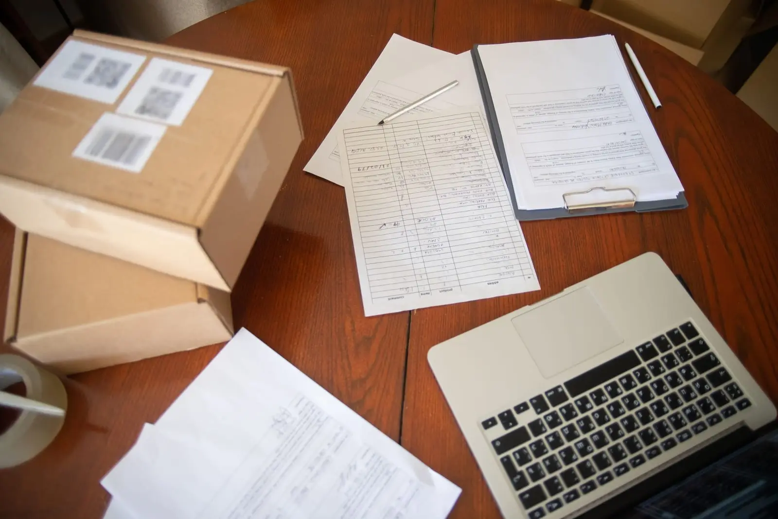 Escritorio con cajas de envío, formatos impresos y un portátil, visto desde arriba