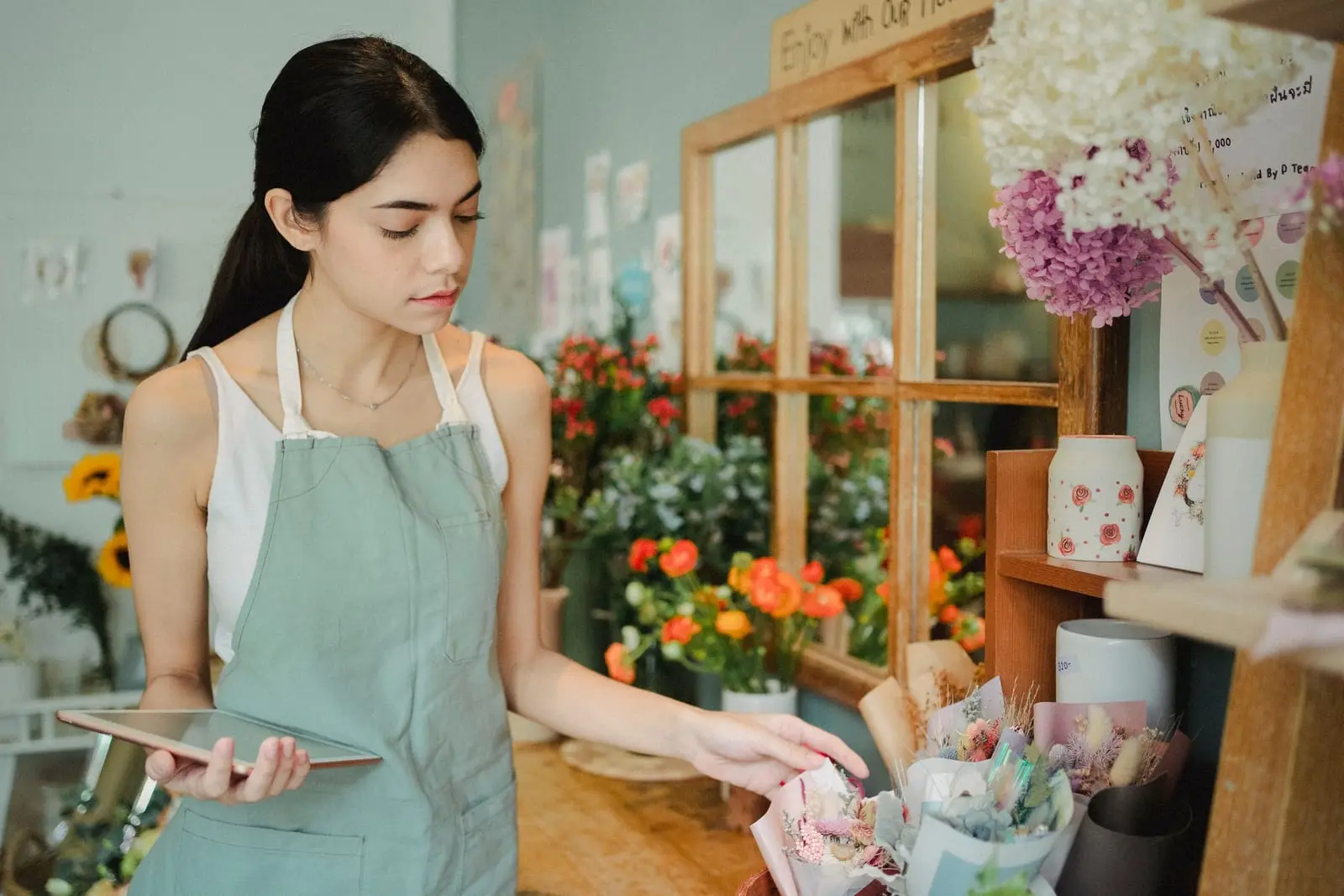 Florista con delantal verde revisa su tableta junto al mostrador de su floristería