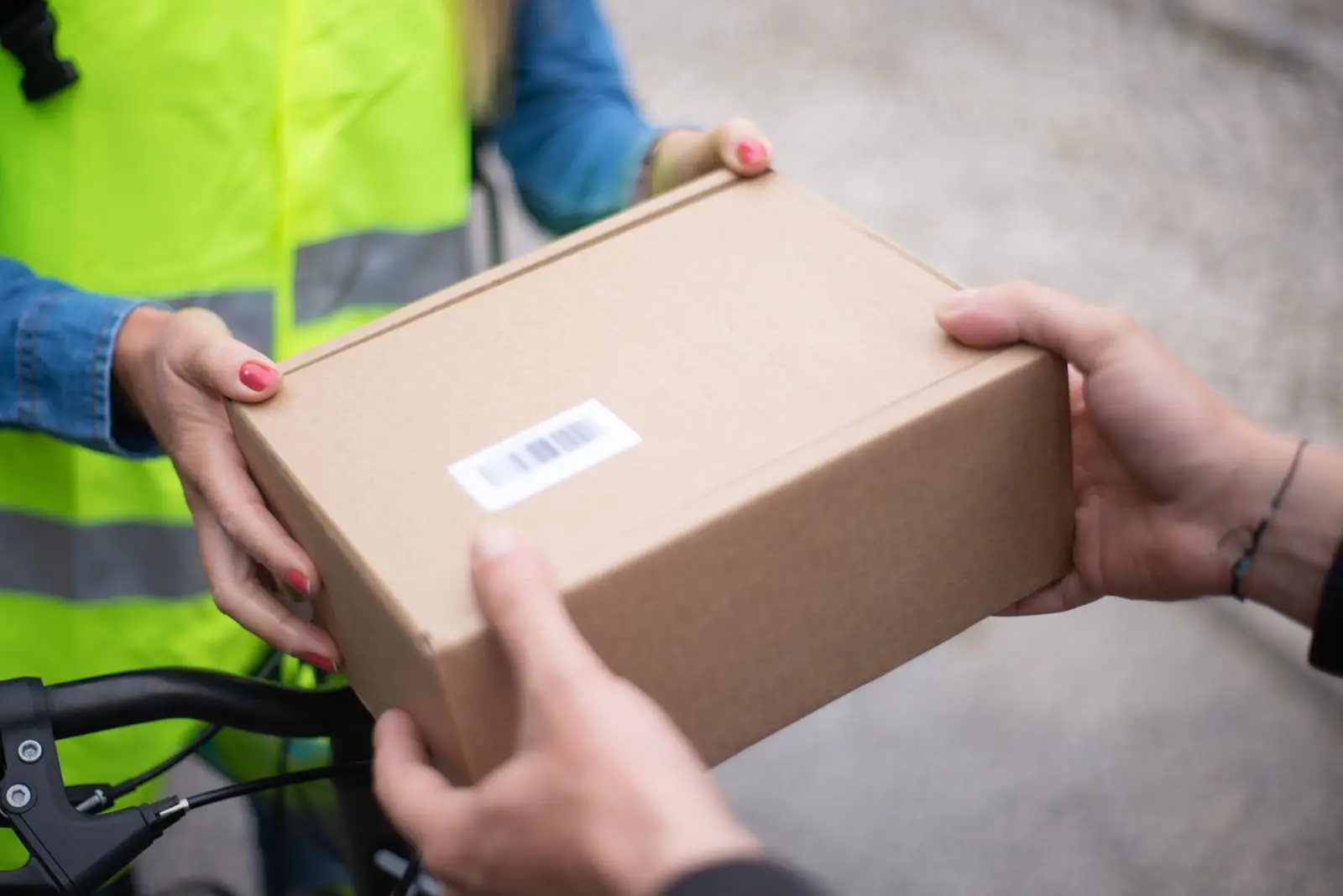 Persona con chaleco reflectivo entrega una caja de cartón con código de barras a otra persona